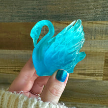 Load image into Gallery viewer, Blue swan-shaped object held by a hand with blue nail polish against a wooden background