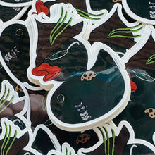 Load image into Gallery viewer, Stack of green rubber duck stickers. The ducks are cosplaying as a witch with a witch hat with a light green feather, holding a biscuit, glasses, and a little gold brooch on her chest. There is a small grey cat next to her. 
