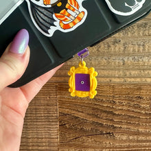 Load image into Gallery viewer, Black E Reader with a yellow friends frame  dust plug. The frame has a purple back and a small peephole in the middle
