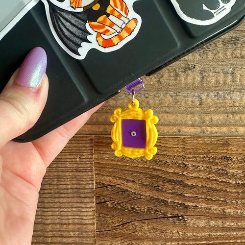Black E Reader with a yellow friends frame  dust plug. The frame has a purple back and a small peephole in the middle
