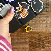 Load image into Gallery viewer, E reader covered in stickers with chocolate frog dust plug in the electric spot. The frog is on a purple back hexagon card with yellow outline swirls. 
